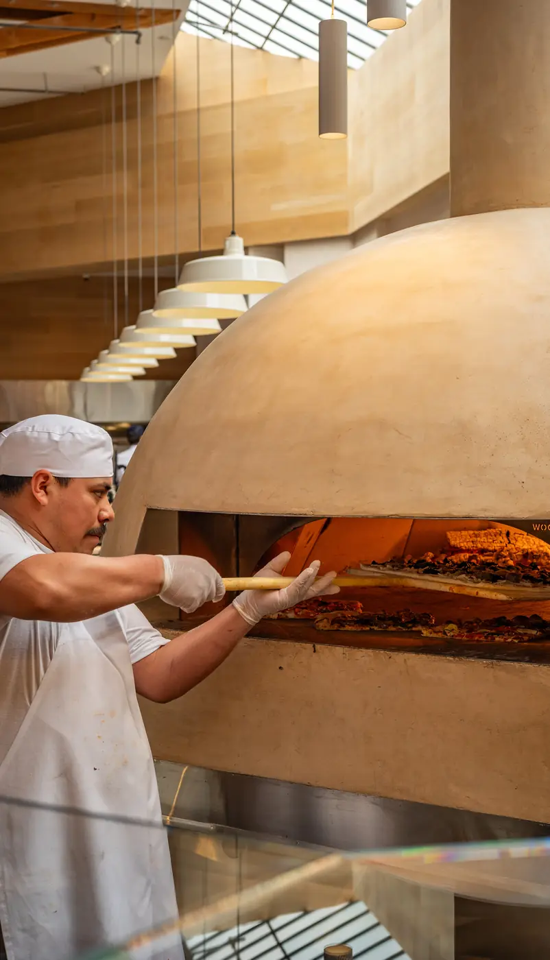 A baker sliding a pizza into the wood-fired oven